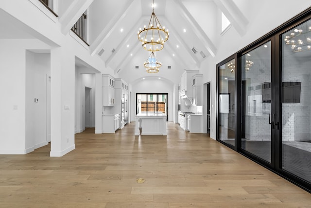 unfurnished living room with a notable chandelier, light hardwood / wood-style floors, and high vaulted ceiling