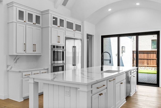 kitchen with sink, white cabinets, light hardwood / wood-style flooring, vaulted ceiling with beams, and a center island with sink