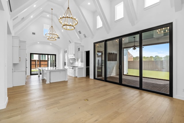 unfurnished living room featuring light wood-type flooring, a notable chandelier, beamed ceiling, and high vaulted ceiling