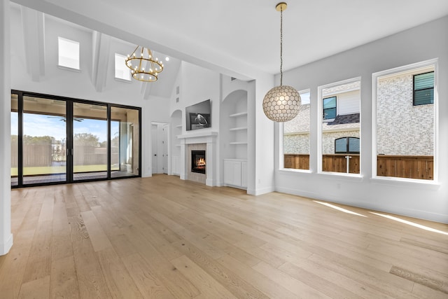 unfurnished living room featuring built in shelves, lofted ceiling, light hardwood / wood-style flooring, a chandelier, and a fireplace