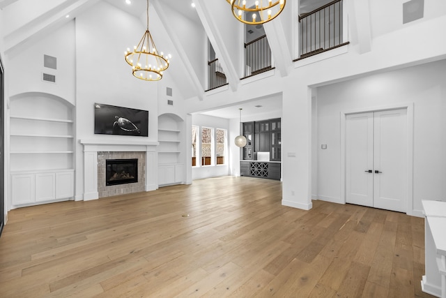 unfurnished living room featuring high vaulted ceiling, a chandelier, light hardwood / wood-style flooring, and a fireplace