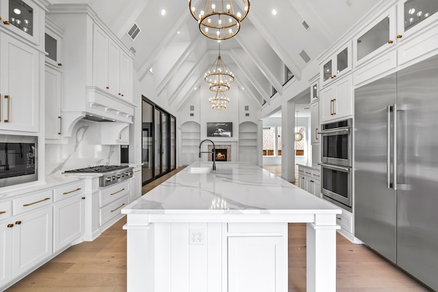 kitchen featuring white cabinets, beam ceiling, a large island with sink, a chandelier, and built in appliances