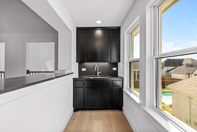 bar with decorative backsplash, light hardwood / wood-style floors, plenty of natural light, and sink