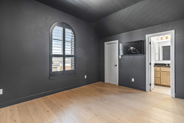 unfurnished bedroom featuring connected bathroom, lofted ceiling, and light hardwood / wood-style floors