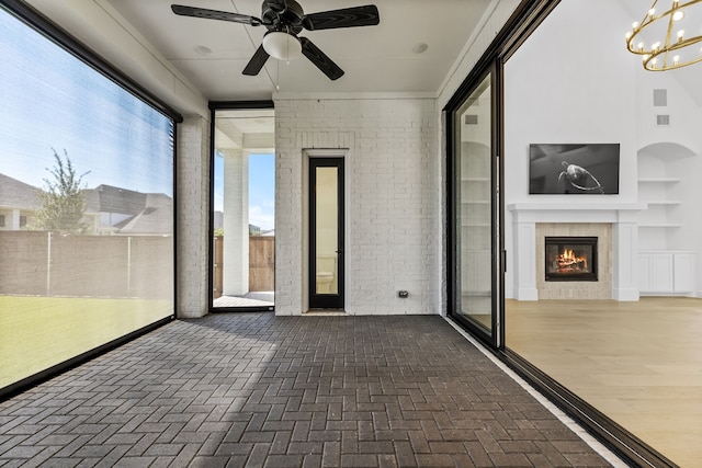 unfurnished sunroom featuring ceiling fan with notable chandelier and a fireplace