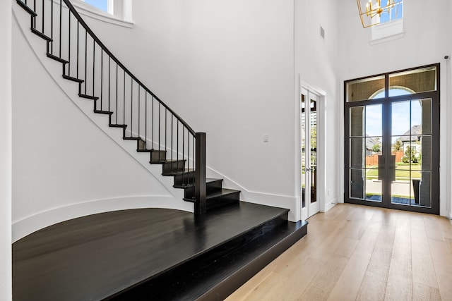 foyer with light wood-type flooring, an inviting chandelier, a towering ceiling, and french doors