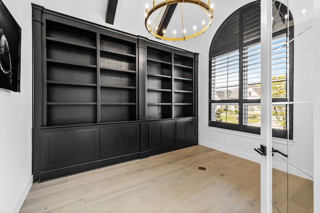 empty room with beamed ceiling, a notable chandelier, and light hardwood / wood-style flooring