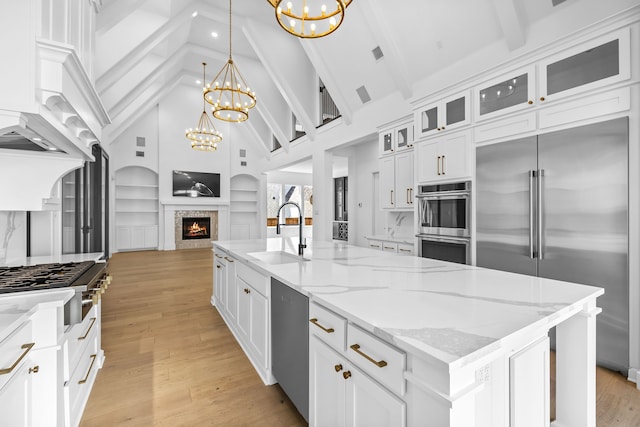 kitchen with hanging light fixtures, stainless steel appliances, a kitchen island with sink, sink, and a chandelier