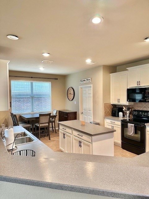 kitchen featuring black appliances, backsplash, a kitchen island, and white cabinets