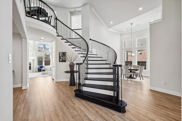 stairs featuring an inviting chandelier, hardwood / wood-style floors, a high ceiling, and crown molding