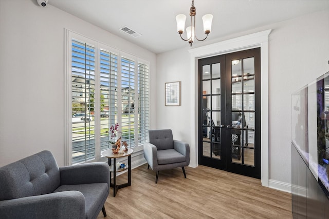 living area with french doors, a notable chandelier, light wood-type flooring, and plenty of natural light