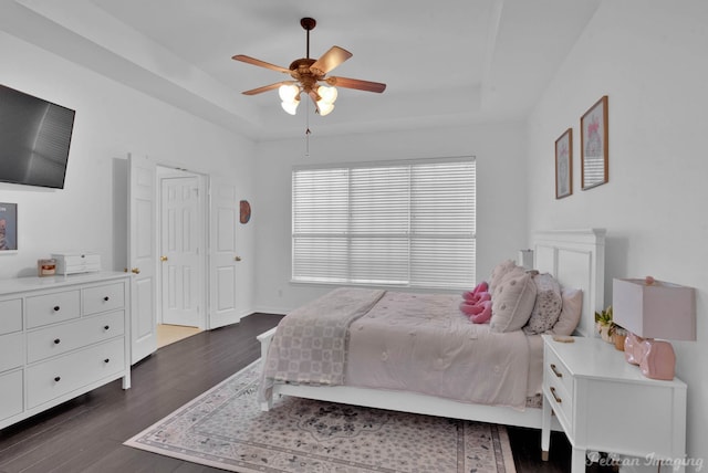 bedroom with ceiling fan, a raised ceiling, and dark wood-type flooring