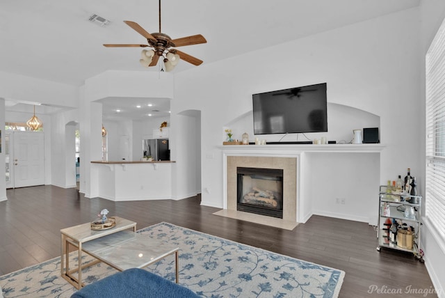 living room featuring dark wood-type flooring, ceiling fan, and a tile fireplace