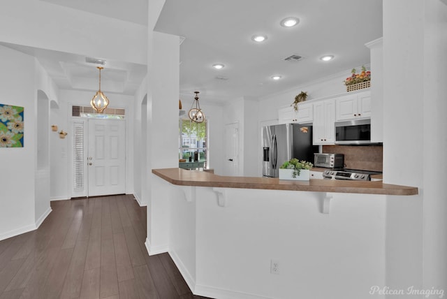 kitchen with kitchen peninsula, hanging light fixtures, white cabinetry, appliances with stainless steel finishes, and a kitchen bar