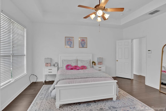 bedroom with ceiling fan, a tray ceiling, and dark hardwood / wood-style floors