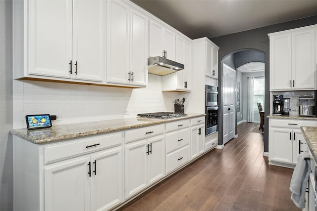 kitchen with appliances with stainless steel finishes, light stone counters, white cabinetry, and dark hardwood / wood-style flooring