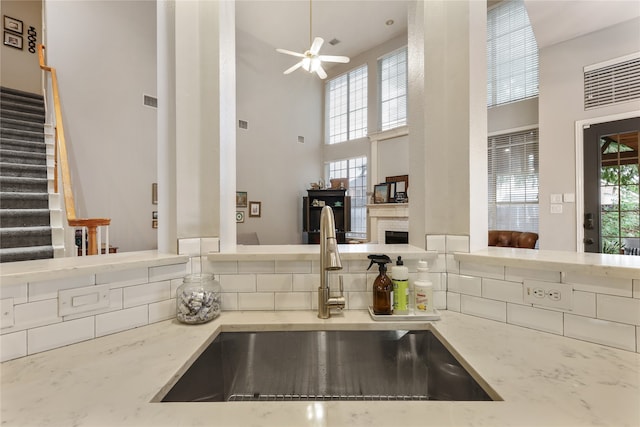 kitchen featuring ceiling fan, sink, a fireplace, a high ceiling, and light stone counters