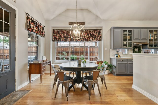 dining room with an inviting chandelier, light hardwood / wood-style flooring, and vaulted ceiling