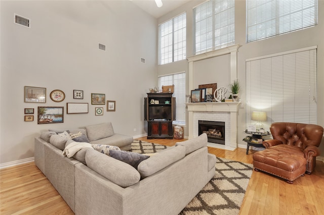 living room featuring light hardwood / wood-style flooring, a brick fireplace, and a high ceiling