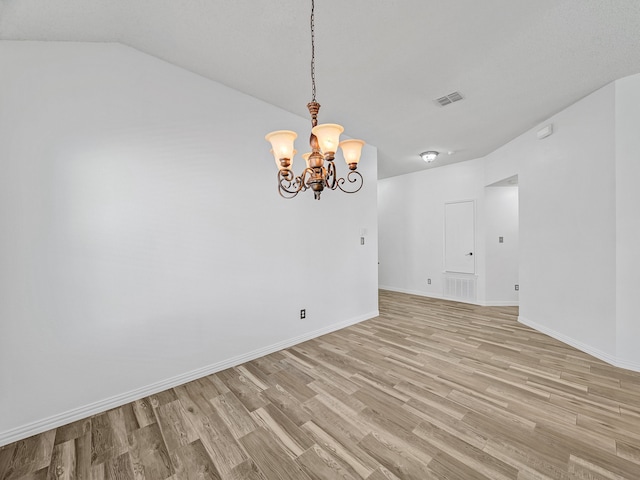 spare room featuring light wood-type flooring, vaulted ceiling, and a notable chandelier