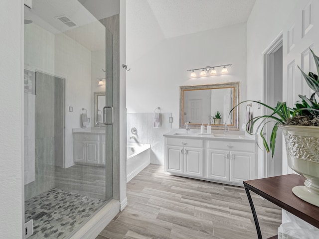 bathroom with vaulted ceiling, vanity, a textured ceiling, separate shower and tub, and hardwood / wood-style floors