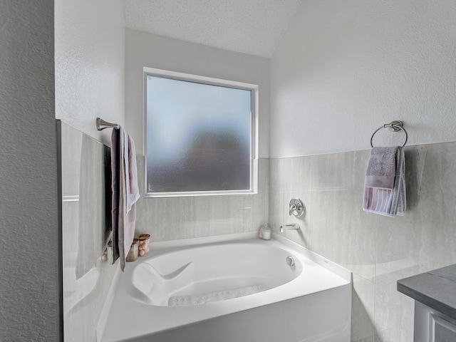 bathroom with vanity, a textured ceiling, tile walls, and a bath