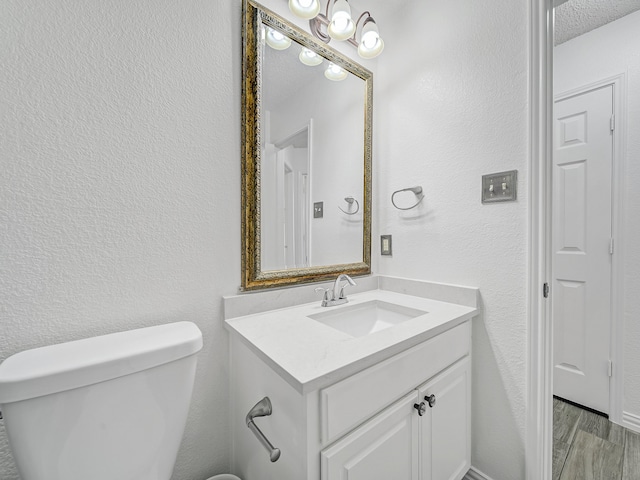 bathroom with a textured ceiling, hardwood / wood-style floors, vanity, and toilet