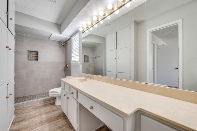 bathroom featuring hardwood / wood-style floors, tiled shower, vanity, and toilet