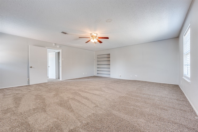 carpeted empty room featuring ceiling fan, a textured ceiling, and built in shelves