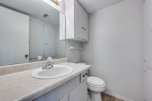 bathroom with wood-type flooring, vanity, toilet, and a textured ceiling