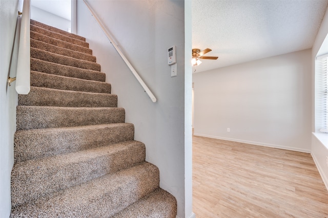 stairway with wood-type flooring, a textured ceiling, and ceiling fan