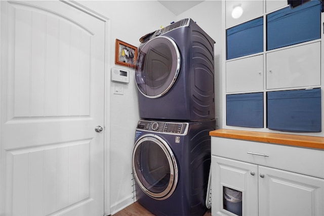 laundry room with cabinets, stacked washer and clothes dryer, and dark wood-type flooring