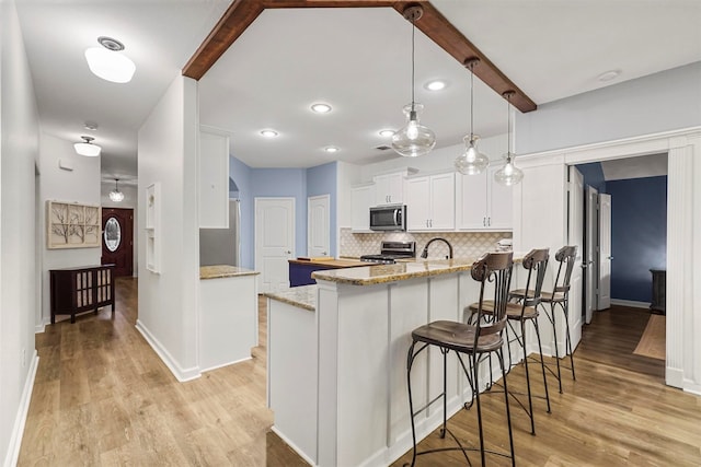 kitchen featuring stainless steel appliances, white cabinetry, kitchen peninsula, hanging light fixtures, and light hardwood / wood-style flooring