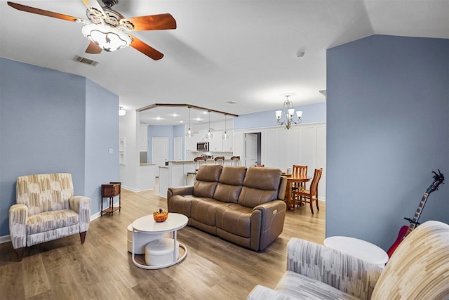 living room with ceiling fan with notable chandelier, light hardwood / wood-style flooring, and vaulted ceiling