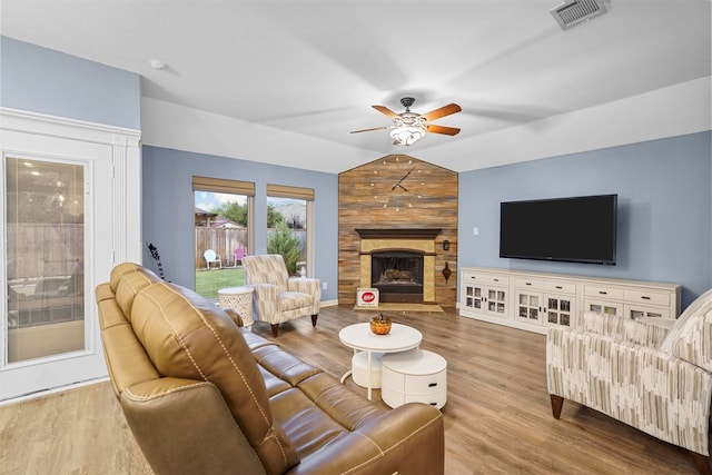 living room featuring vaulted ceiling, wooden walls, hardwood / wood-style flooring, ceiling fan, and a fireplace