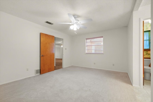 unfurnished bedroom with ceiling fan, a textured ceiling, ensuite bath, and light carpet