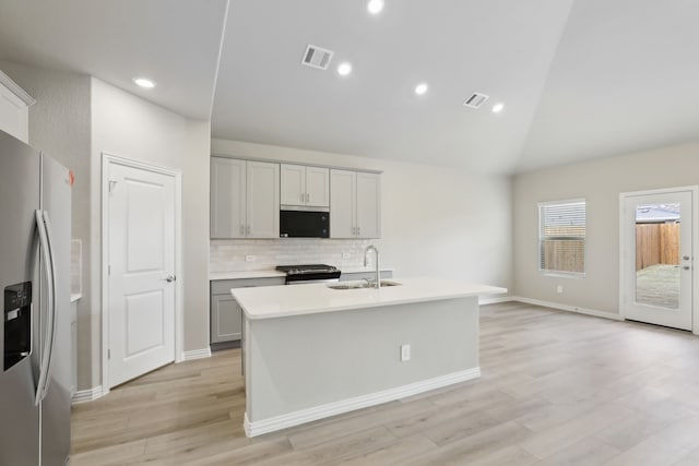 kitchen with sink, stainless steel appliances, gray cabinets, an island with sink, and tasteful backsplash