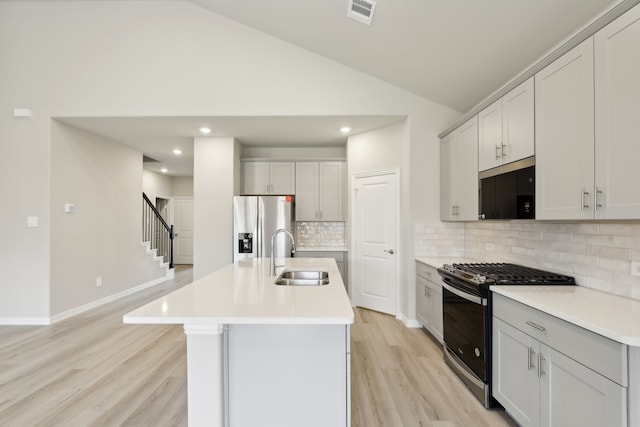 kitchen with an island with sink, lofted ceiling, stainless steel appliances, light hardwood / wood-style floors, and sink