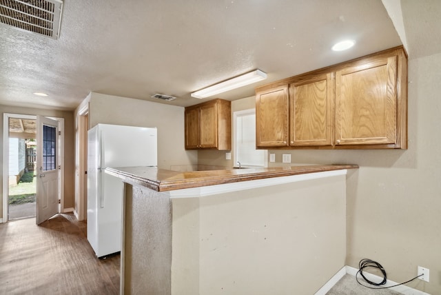 kitchen with kitchen peninsula, white refrigerator, dark wood-type flooring, and a textured ceiling