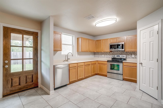 kitchen featuring light tile patterned flooring, sink, tasteful backsplash, stainless steel appliances, and light brown cabinetry