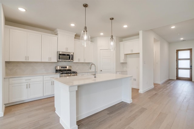 kitchen featuring a kitchen island with sink, light hardwood / wood-style flooring, stainless steel appliances, decorative light fixtures, and white cabinetry