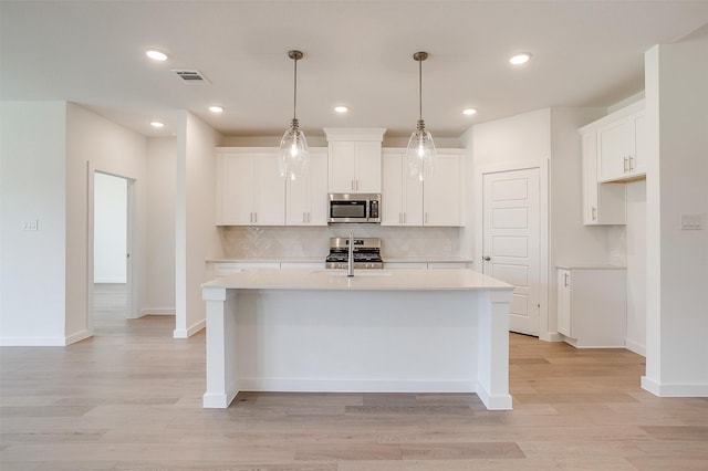 kitchen with appliances with stainless steel finishes, decorative light fixtures, white cabinets, and an island with sink