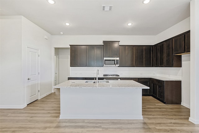 kitchen with decorative light fixtures, light hardwood / wood-style floors, a kitchen breakfast bar, and a kitchen island with sink