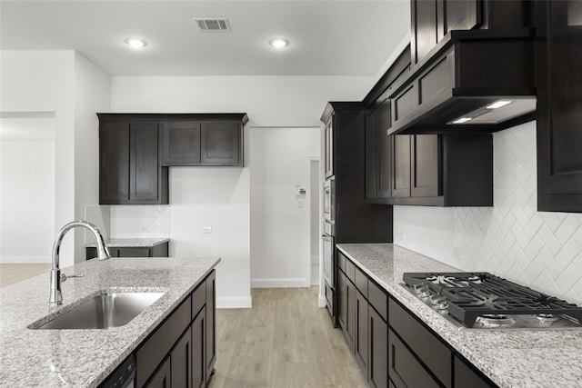 kitchen with backsplash, sink, light hardwood / wood-style flooring, light stone counters, and stainless steel gas cooktop