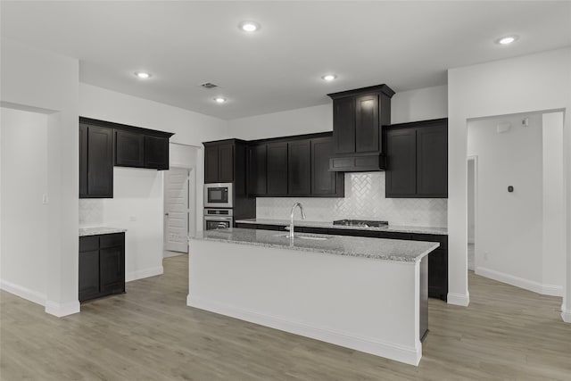 733 Lemmon Ln, Forney, TX 75126 - kitchen featuring light wood finished floors, a sink, a center island with sink, tasteful backsplash, and appliances with stainless steel finishes