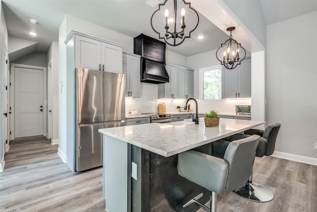 kitchen with decorative light fixtures, light stone countertops, an island with sink, and appliances with stainless steel finishes