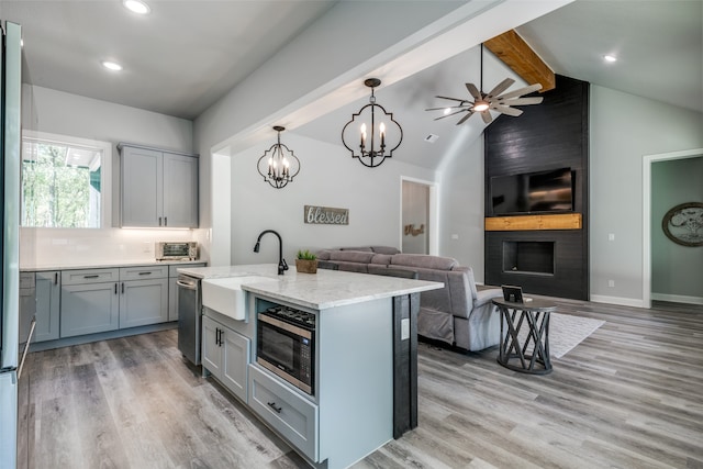 kitchen with stainless steel appliances, a kitchen island with sink, lofted ceiling with beams, light hardwood / wood-style flooring, and a fireplace