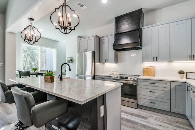 kitchen featuring gray cabinetry, light wood-type flooring, an island with sink, light stone counters, and stainless steel appliances