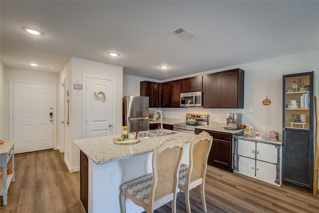 kitchen featuring dark brown cabinetry, sink, a kitchen island with sink, light hardwood / wood-style flooring, and appliances with stainless steel finishes