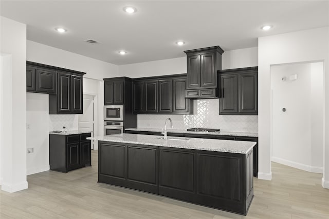 kitchen with a kitchen island with sink, sink, light hardwood / wood-style flooring, appliances with stainless steel finishes, and light stone counters